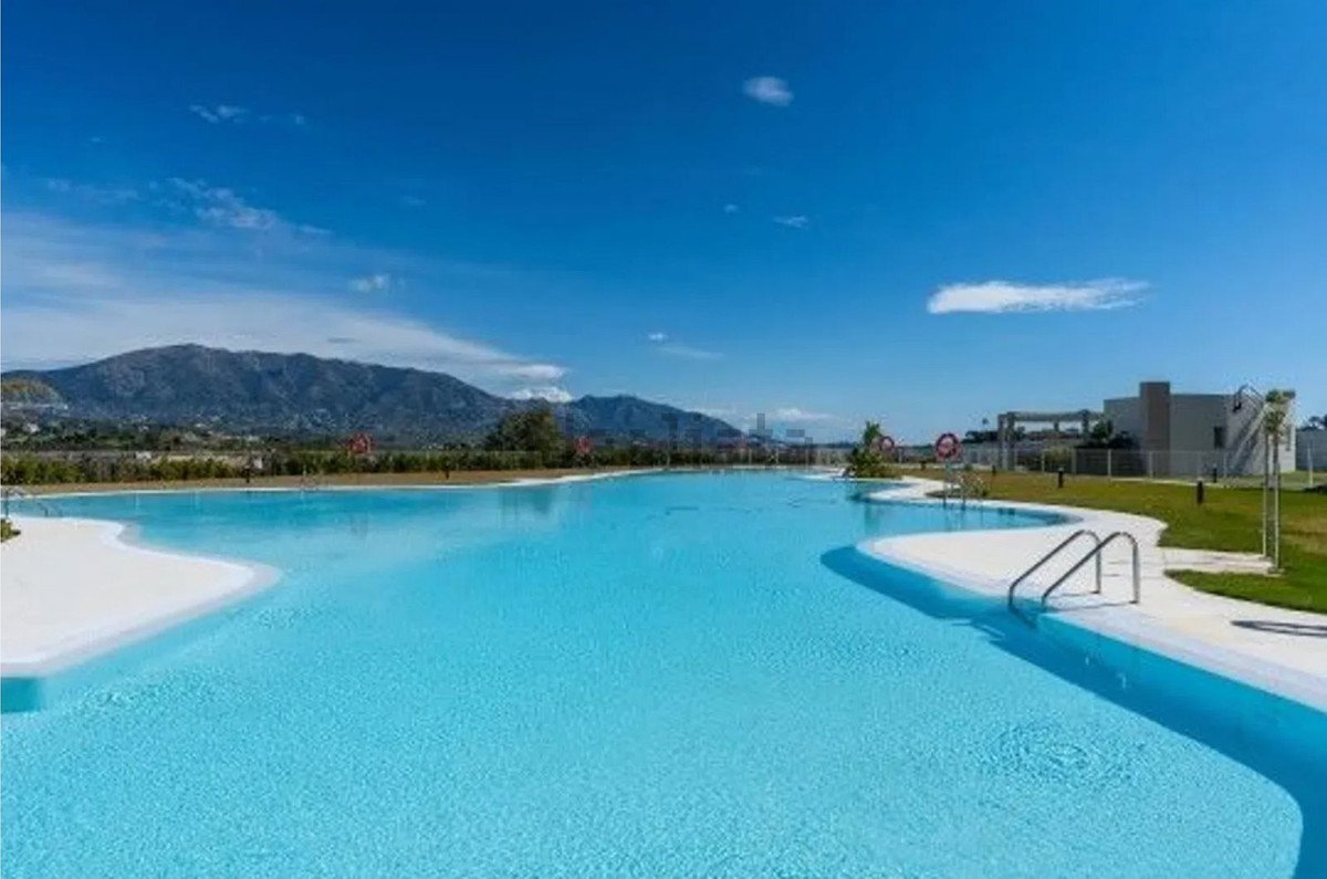 Spacious resort-style pool with white sandy edges and a mountain backdrop under a clear blue sky.