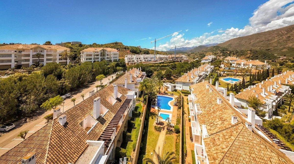 Aerial view of a resort complex with apartments, swimming pools, gardens, and mountains in the background.