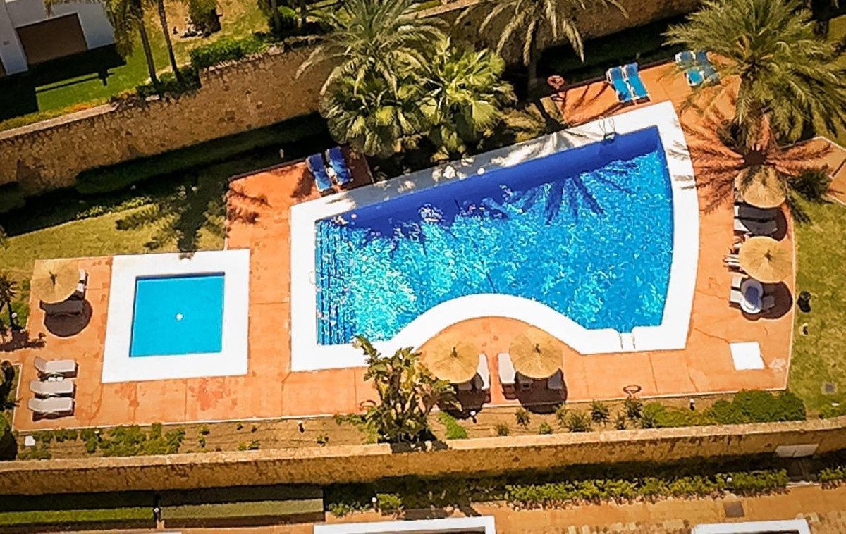 Aerial view of a resort villa's outdoor area featuring a large swimming pool, a smaller plunge pool, sun loungers, and palm trees.