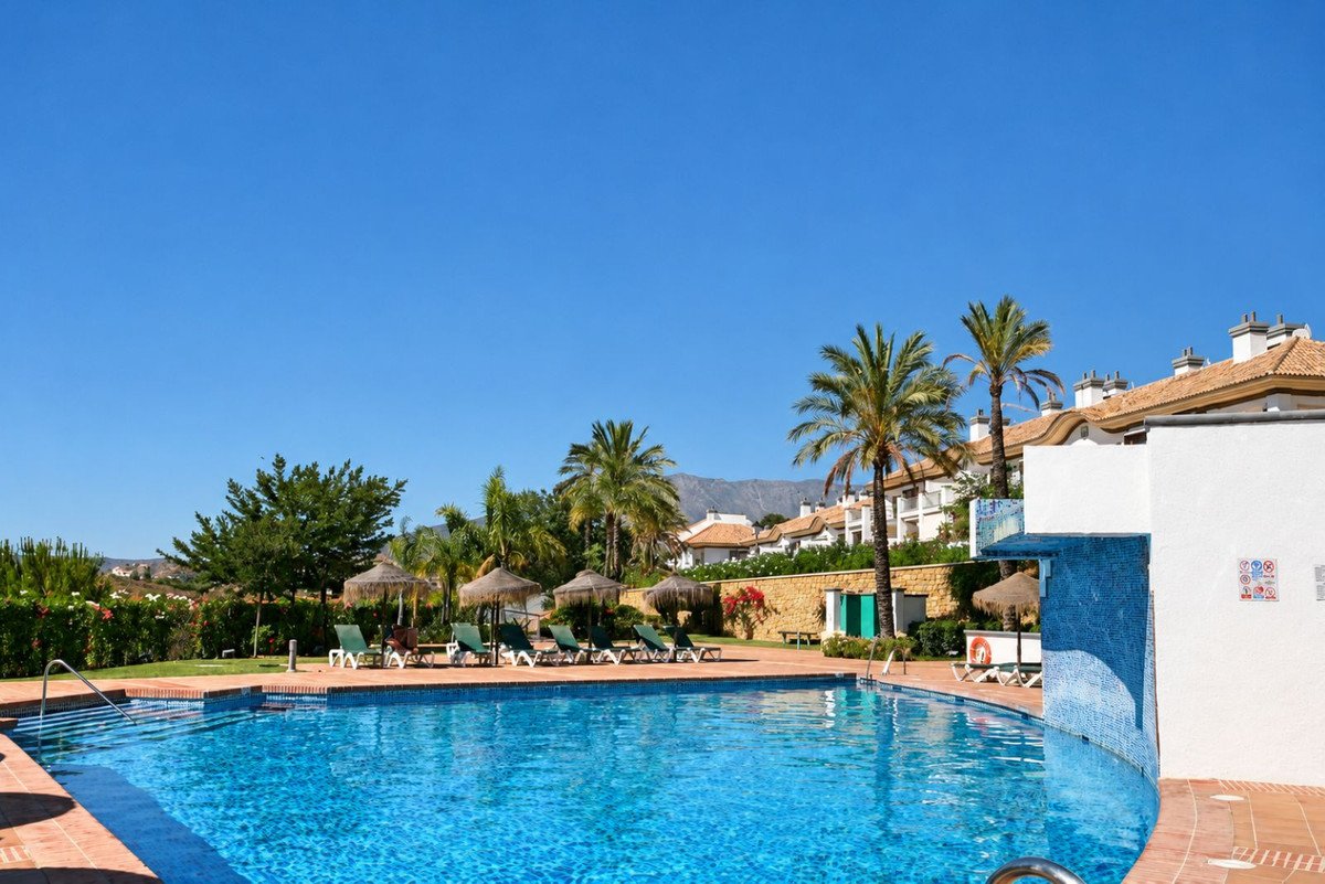 Swimming pool with lounge chairs, palm trees, and resort buildings under clear blue sky