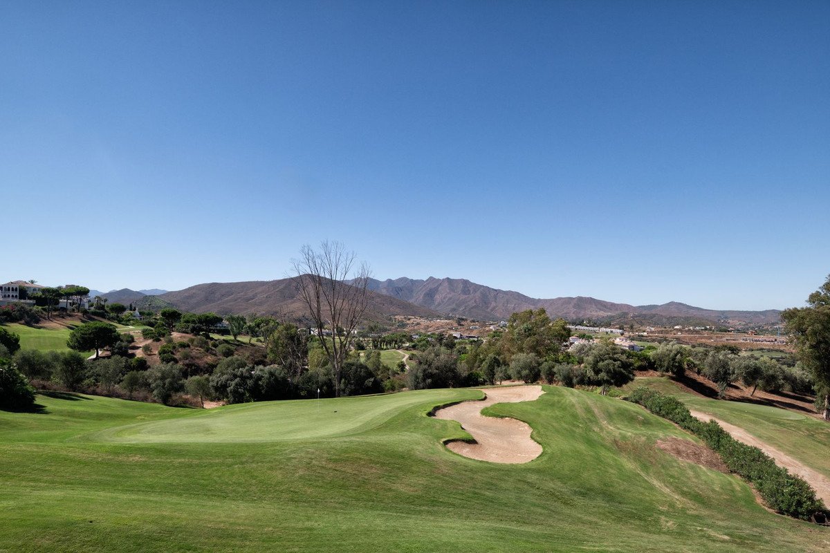 Golf course with sand traps and mountain landscape under blue sky