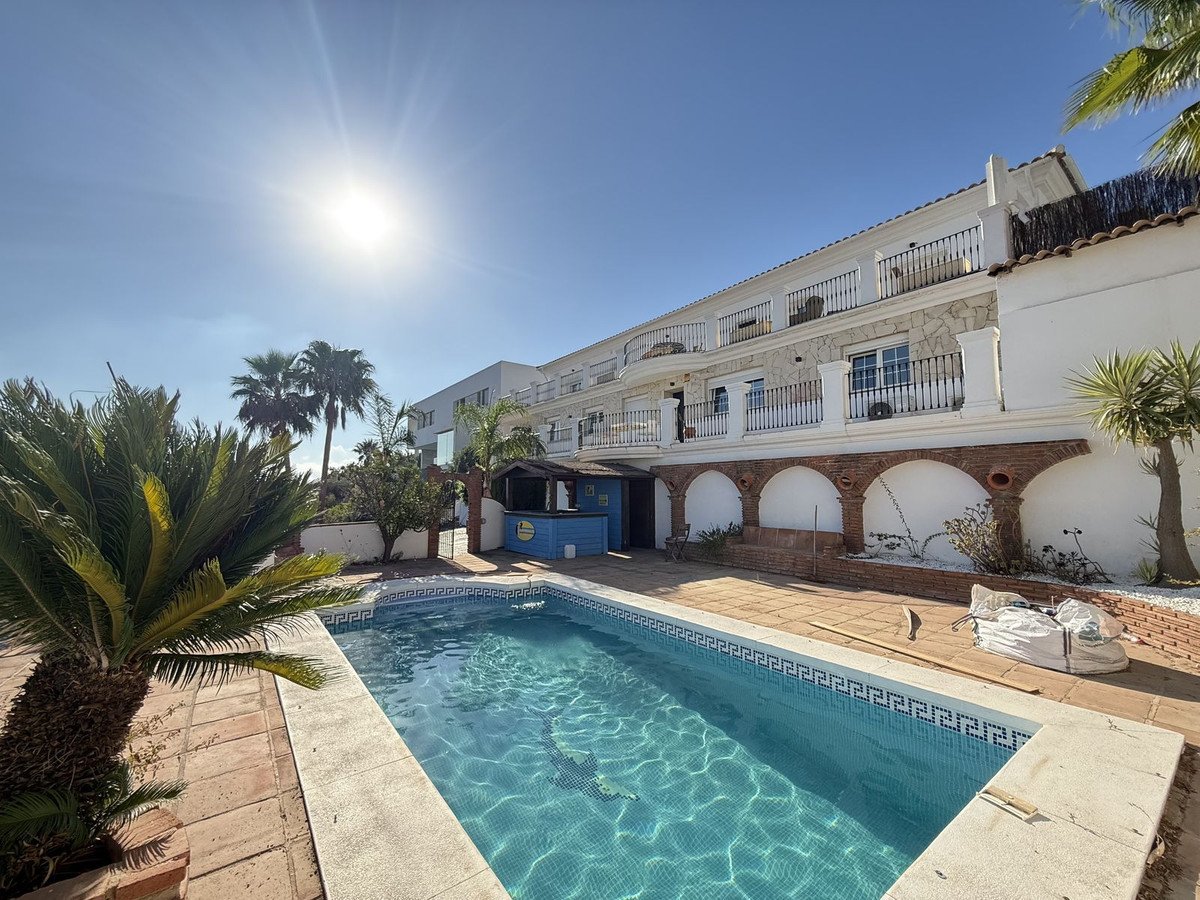 A sunny day at a villa with a swimming pool, palm trees, and balconies.