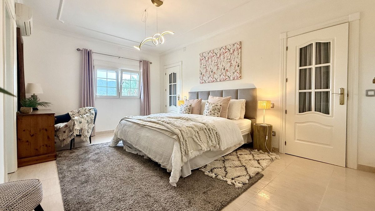 A spacious bedroom with a large bed, soft furnishings, and windows offering a view of rolling green hills.