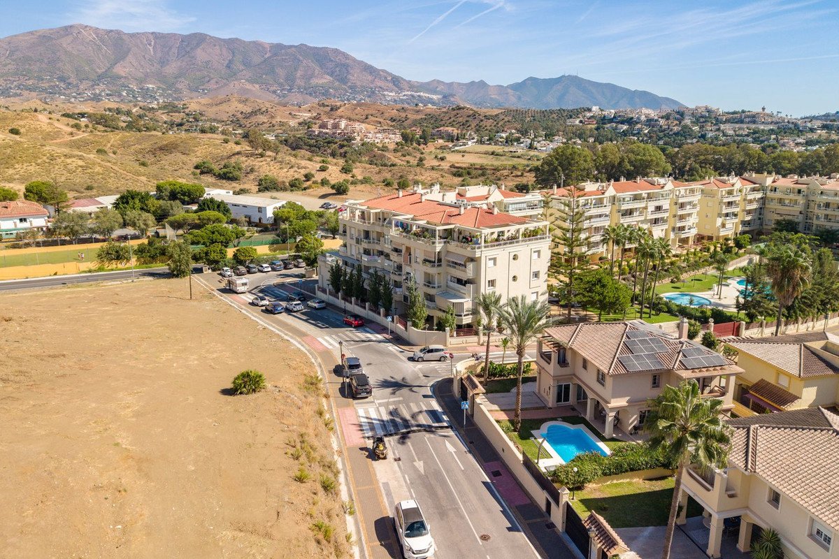 Aerial view of a modern apartment complex with balconies, overlooking a swimming pool and mountains in the distance.