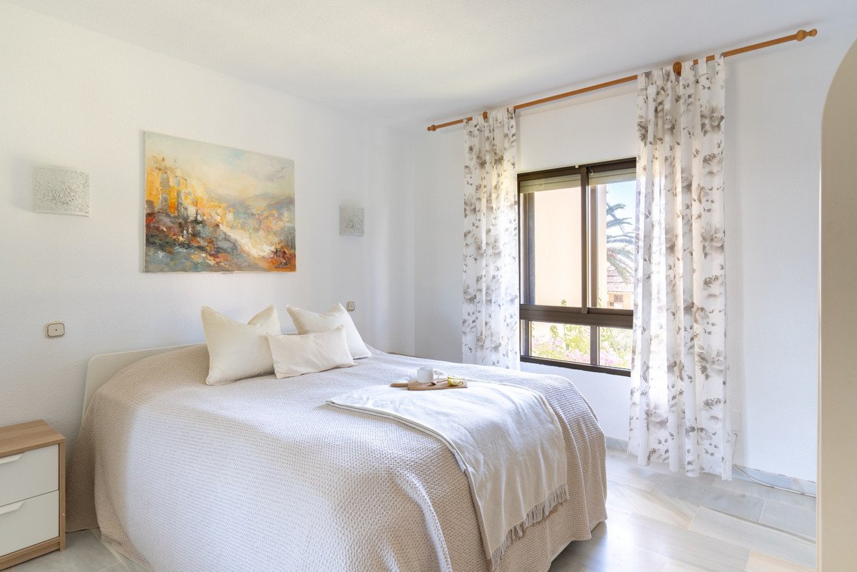 A bright bedroom with a bed, floral curtains, and a window view of palm trees.
