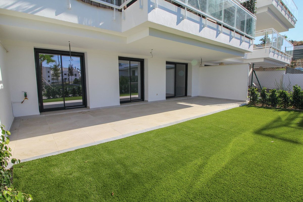 A modern building exterior featuring a spacious terrace with artificial grass lawn, large sliding glass doors, and balconies above.