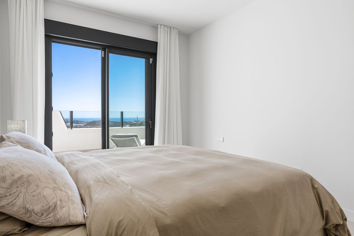 Bedroom with large sliding glass doors opening to a balcony with sea view and a lounge chair.