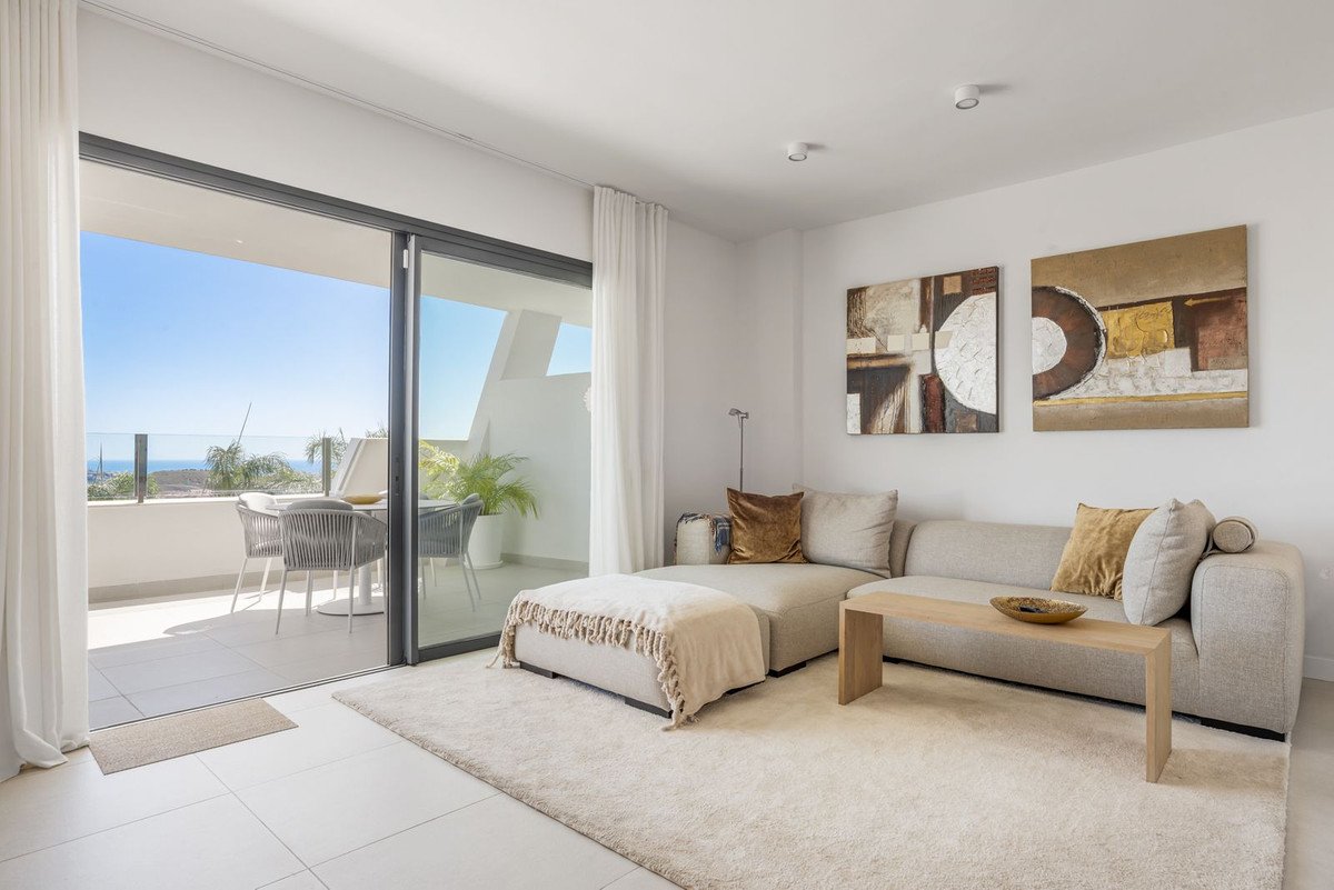 Modern living room with beige sofa, ottoman, and large sliding doors opening to a balcony with sea view.