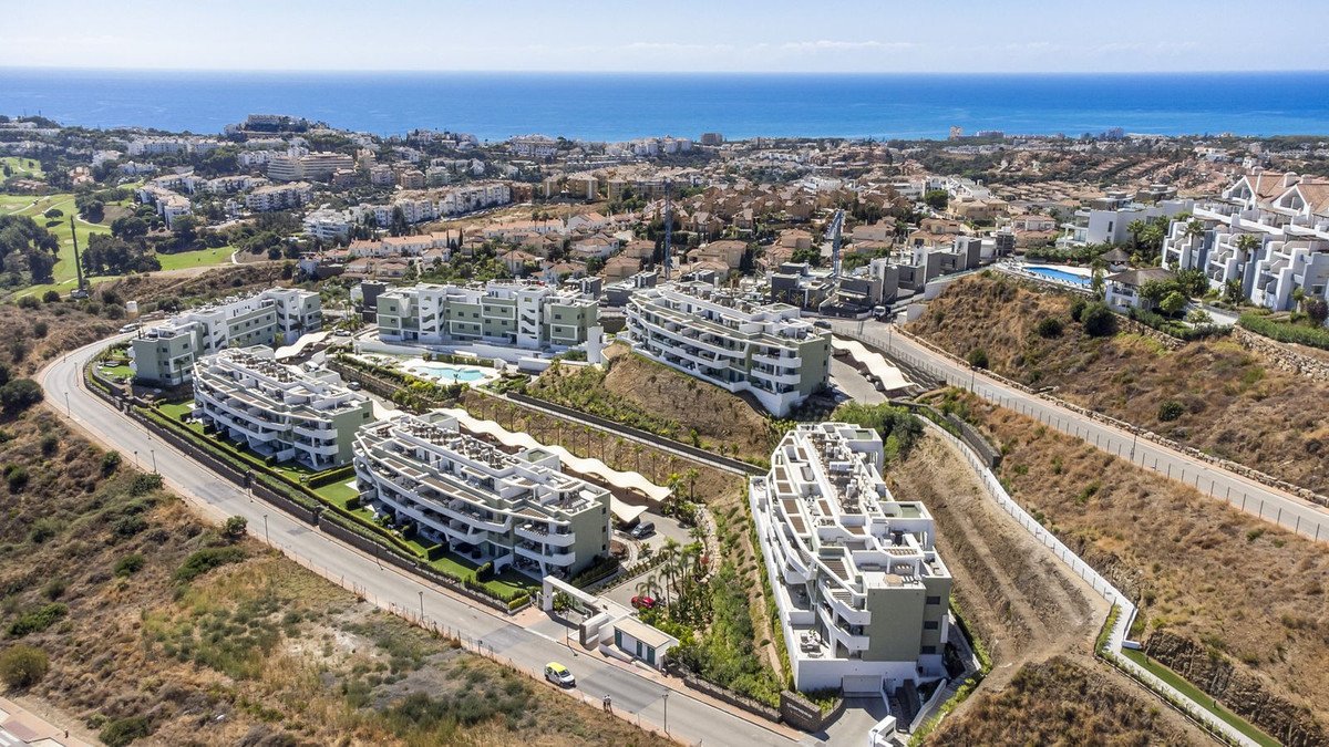 Modern apartment buildings on a hillside overlooking the sea, with swimming pool and golf course nearby.