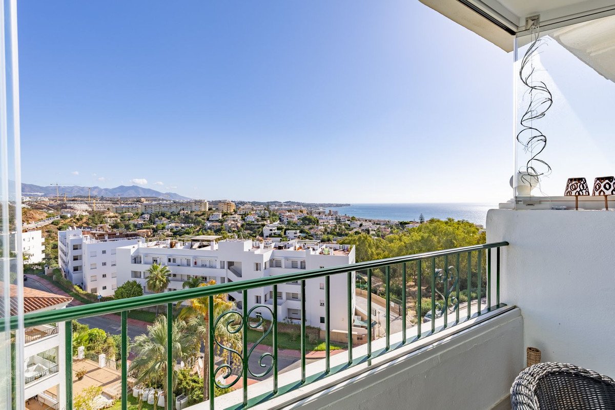 Balcony overlooking a coastal town with the sea and mountains in the distance under a clear blue sky.