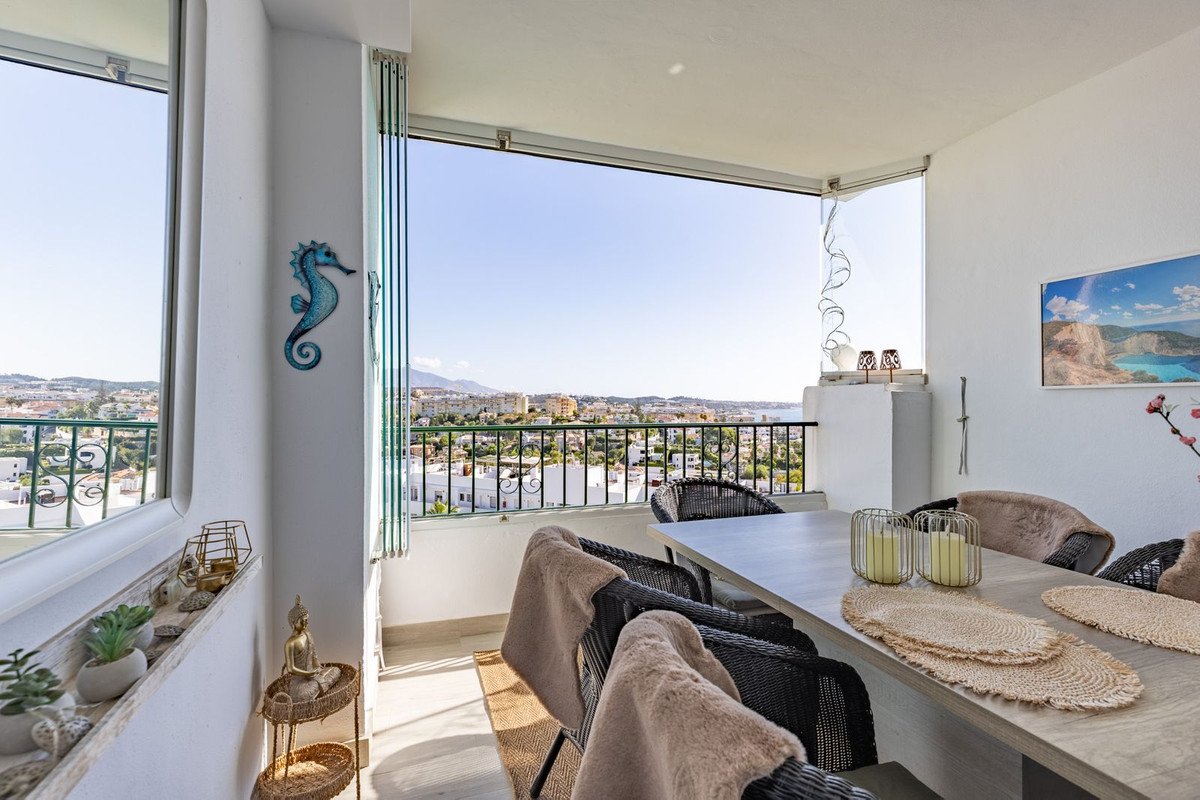 Dining area on a balcony with a table and chairs, overlooking a town and the sea.