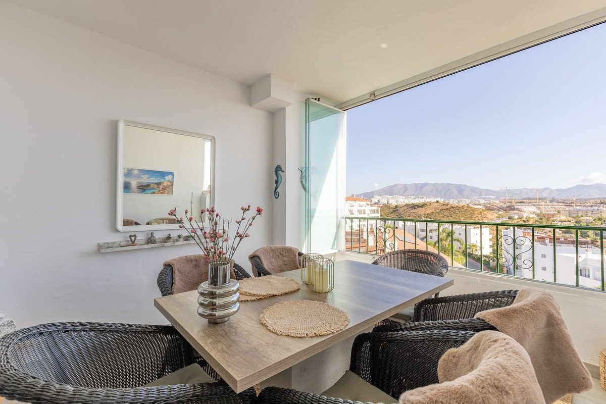 Spacious balcony with dining set and chairs, overlooking a town and mountains with a clear blue sky.