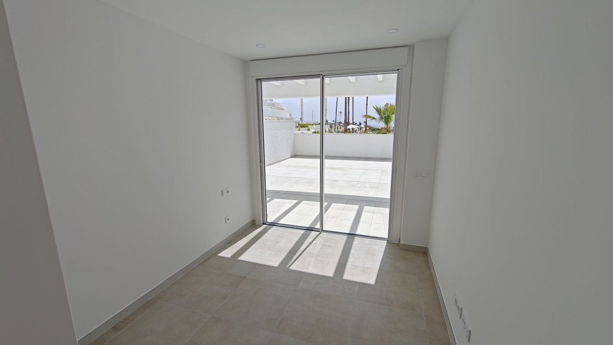 Interior room with sliding glass doors leading to a tiled terrace with palm trees and a distant sea view.