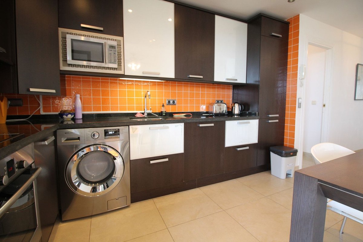 Modern kitchen featuring white and brown cabinets, orange tiled backsplash, and stainless steel appliances