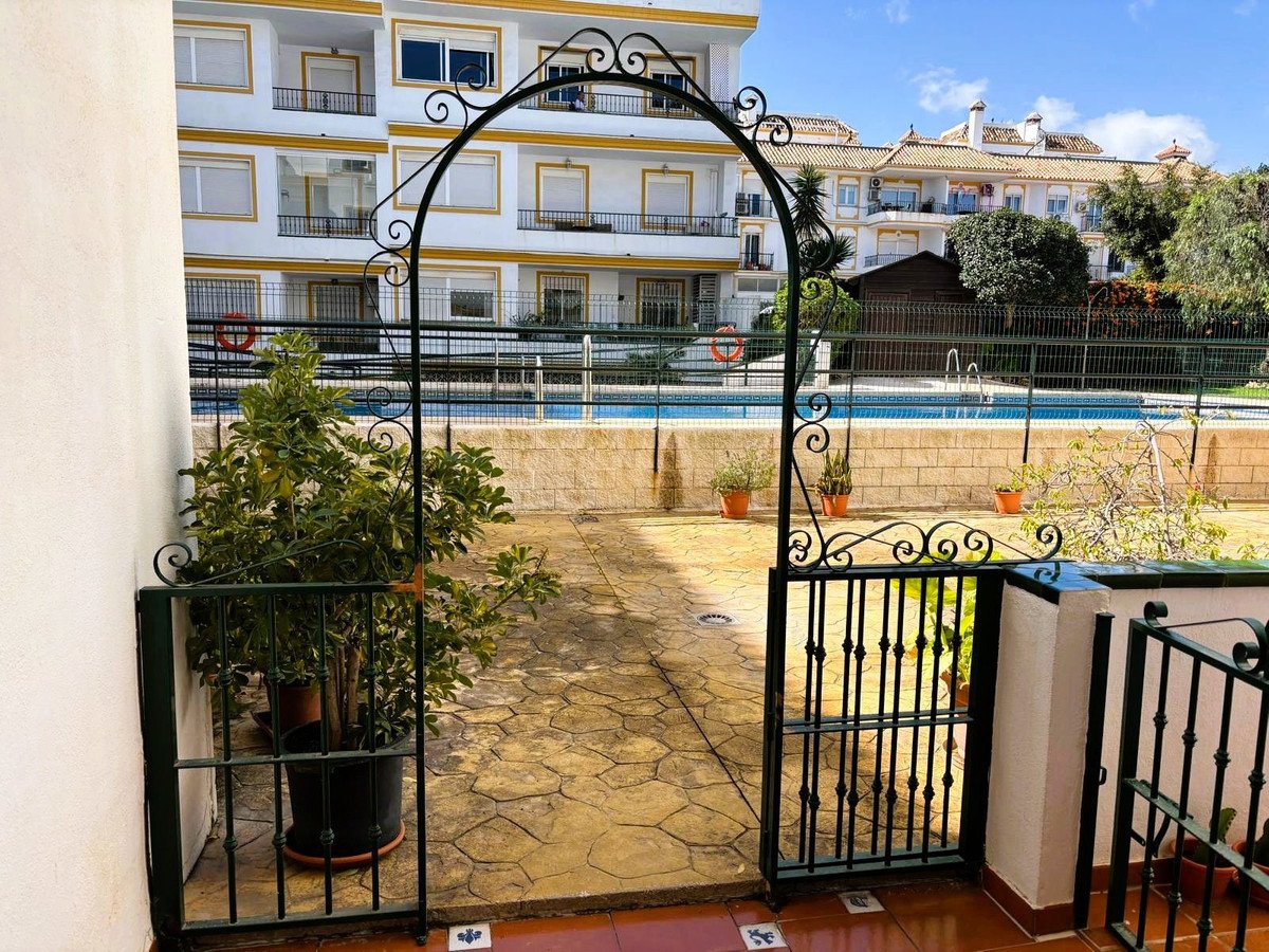 A patio area with a wrought iron gate leads to a swimming pool and apartment buildings.