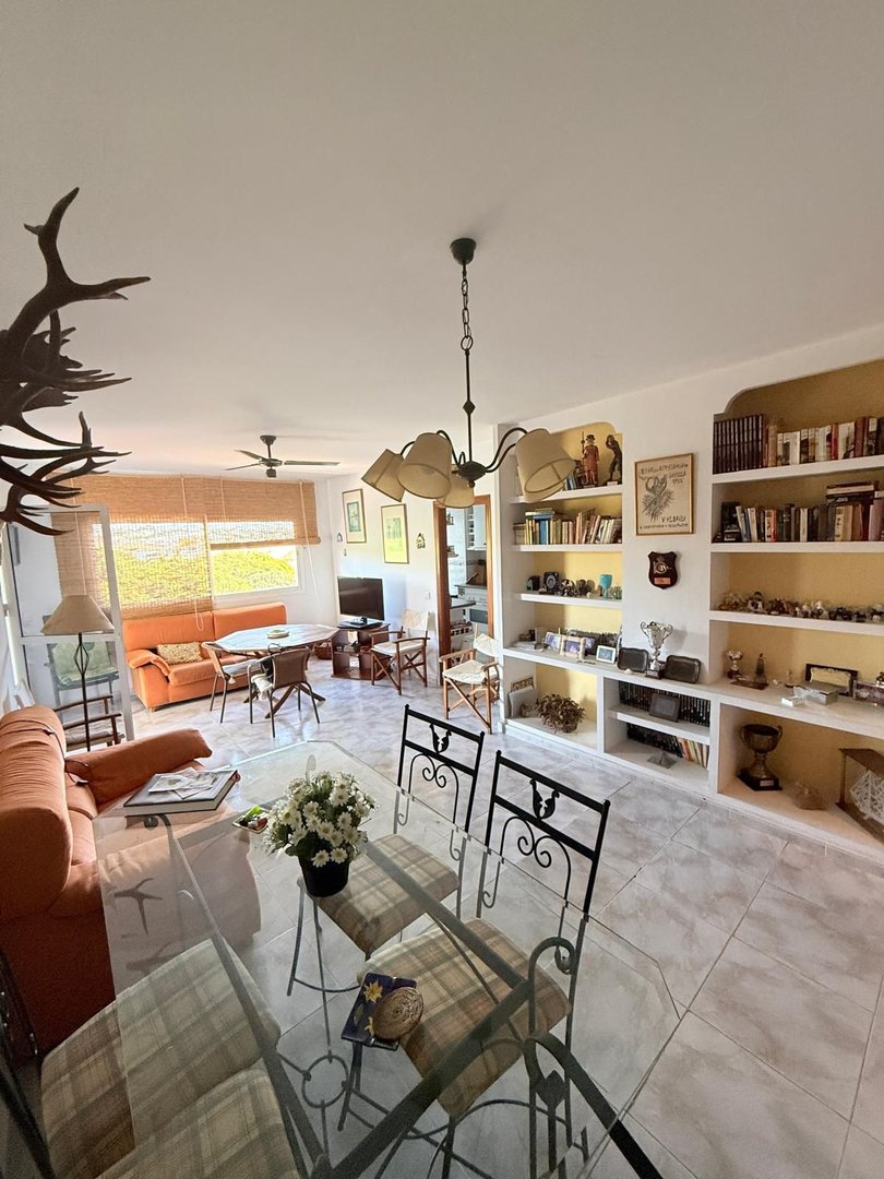A spacious living and dining room with orange sofas, a glass dining table, and extensive built-in shelving filled with decor.