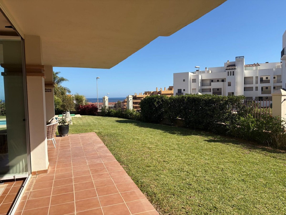 Terrace and garden with sea view, featuring a well-maintained lawn and modern apartment buildings in the background.