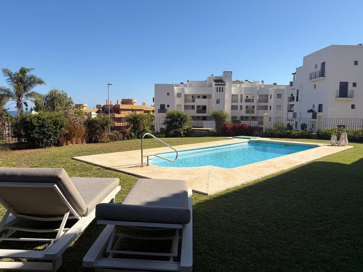 Private swimming pool with sun loungers in front of white apartment buildings on a sunny day.