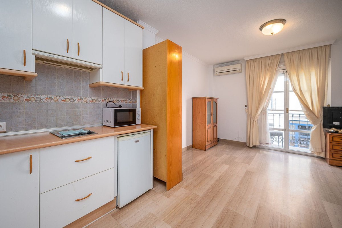 A studio apartment with a kitchenette, a wooden cabinet, and a balcony with a view of the street below.