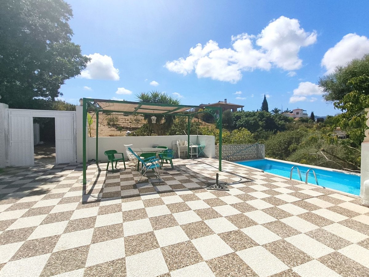 A sunny patio with a swimming pool, outdoor dining area, and green chairs under a pergola.