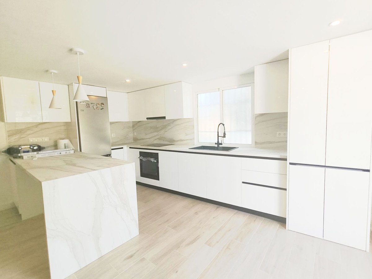 A modern white kitchen with a marble island, sleek cabinets, a black faucet, and stainless steel appliances.