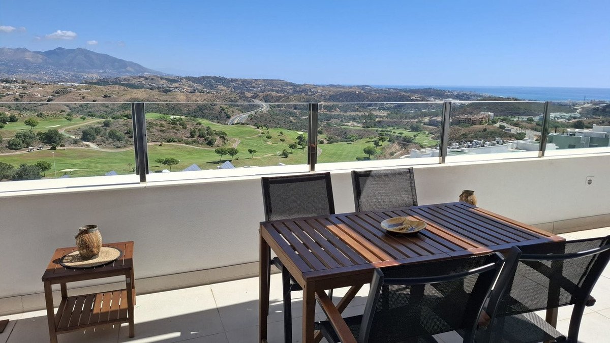 Terrace with dining table and chairs overlooking a golf course with distant sea and mountain views.