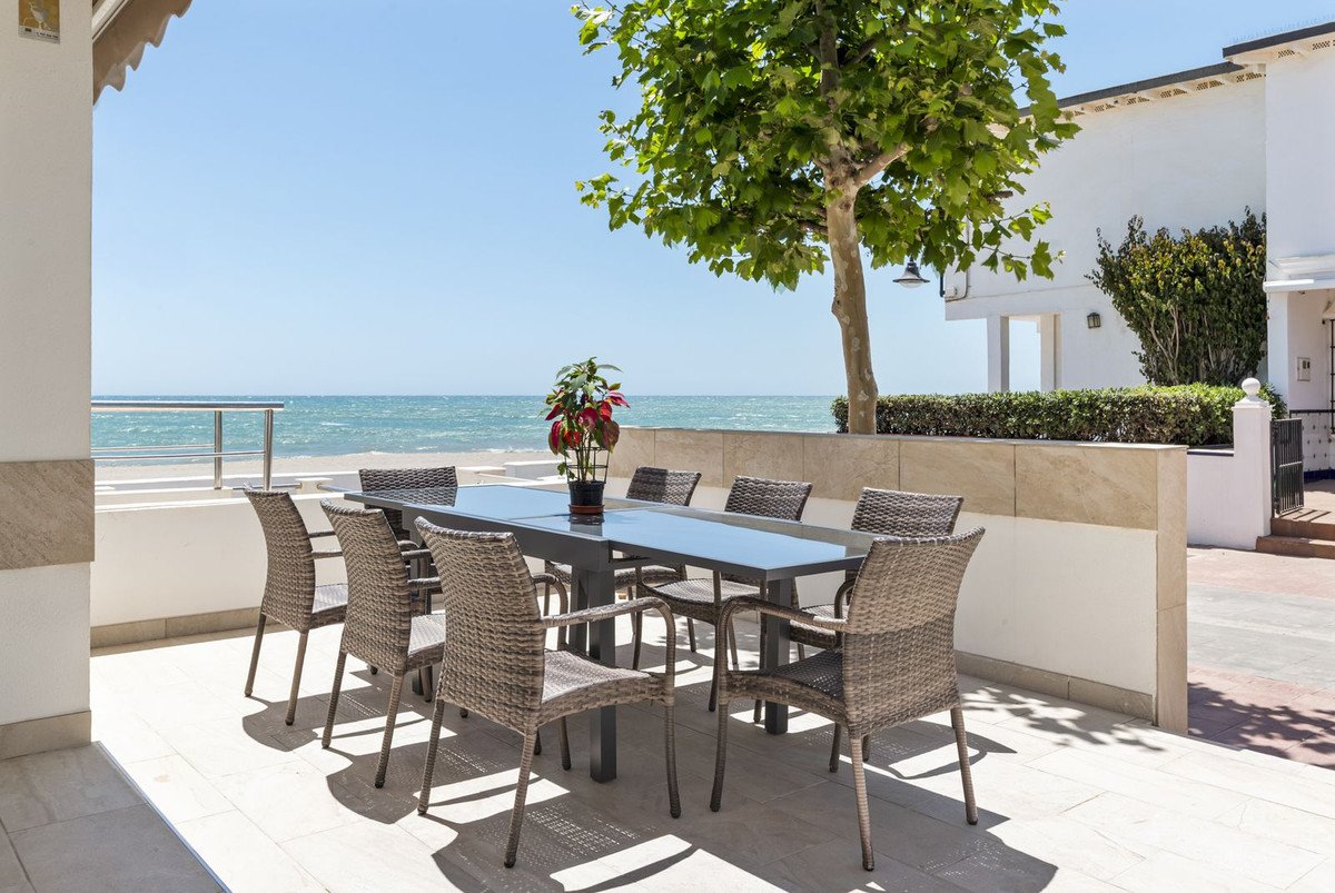 Terrace with dining table and chairs overlooking the sea and beach on a sunny day.