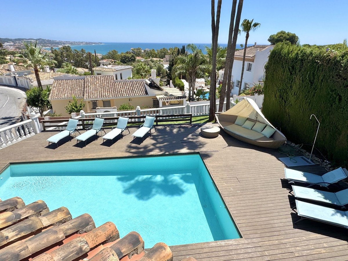 Outdoor swimming pool and wooden deck with lounge chairs and sea view.