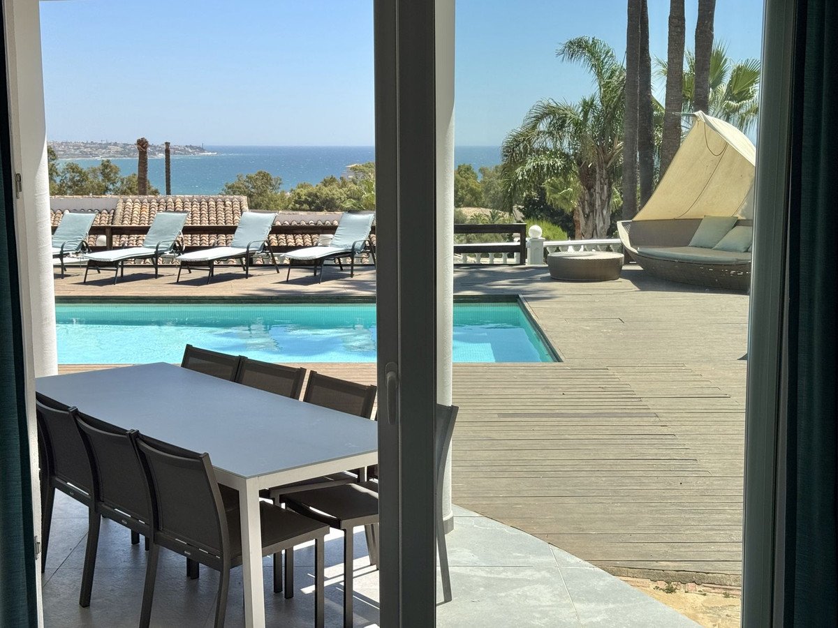 Luxurious outdoor dining area and pool with sun loungers and a shaded daybed, overlooking the sea.