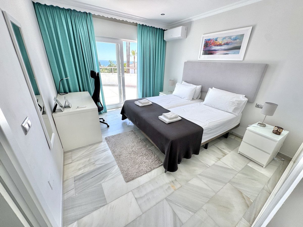 A bedroom with two beds, a desk, a balcony, and a sea view through turquoise curtains.