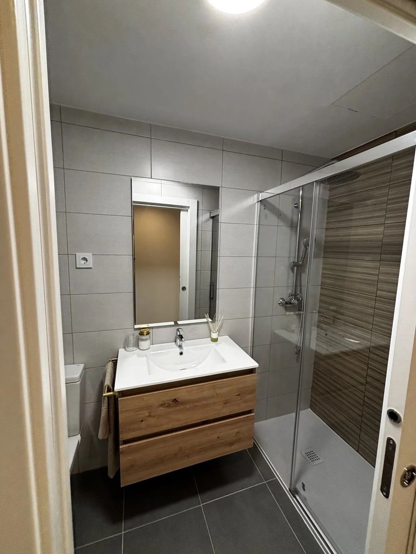 Modern bathroom with a floating wood vanity, white sink, large mirror, and a glass-enclosed shower with tiled walls.