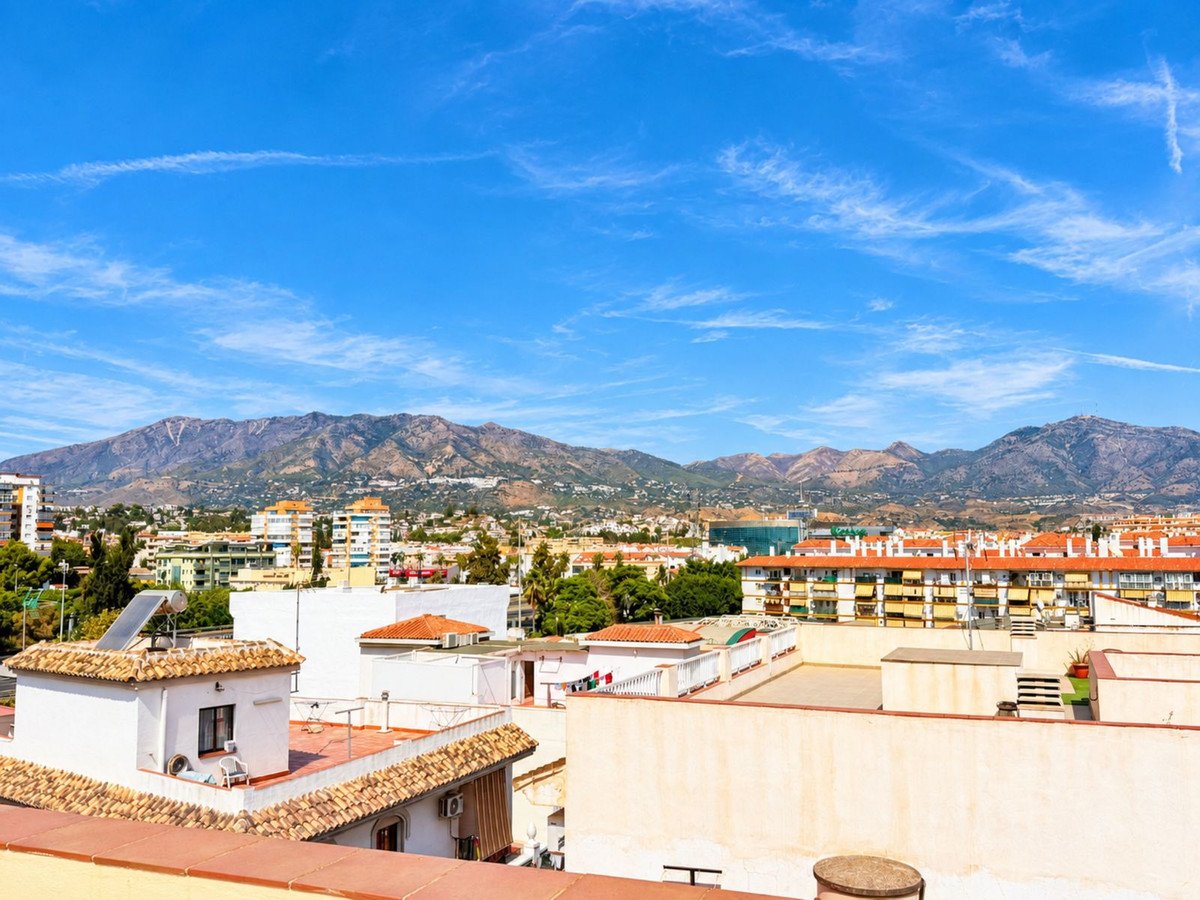 A panoramic view from a rooftop terrace overlooking a town with mountains in the background under a blue sky.