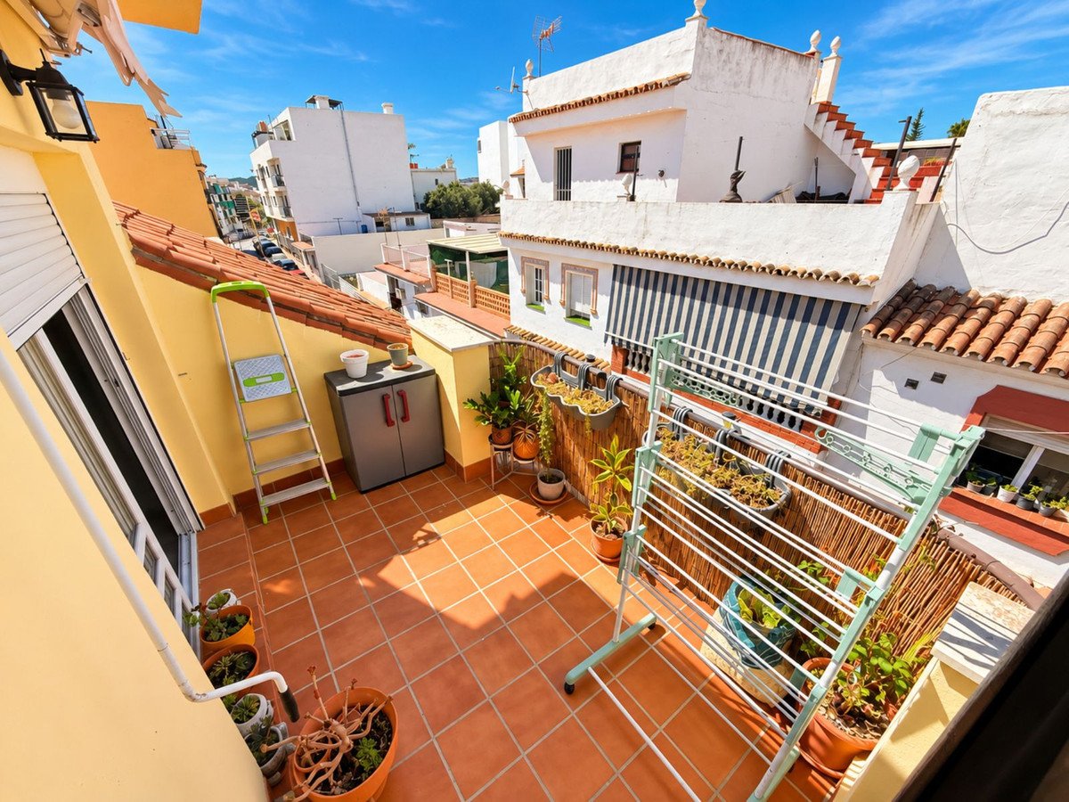 Sunny terrace with terracotta tiles, potted plants, clothes drying rack, and buildings in the background.