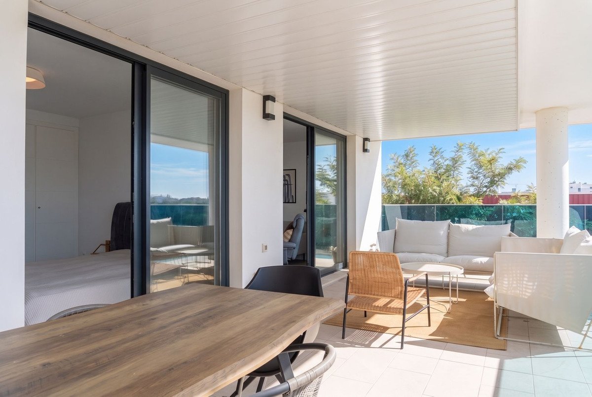 Spacious balcony with dining table and seating area, overlooking the sea and lush greenery under a clear blue sky.