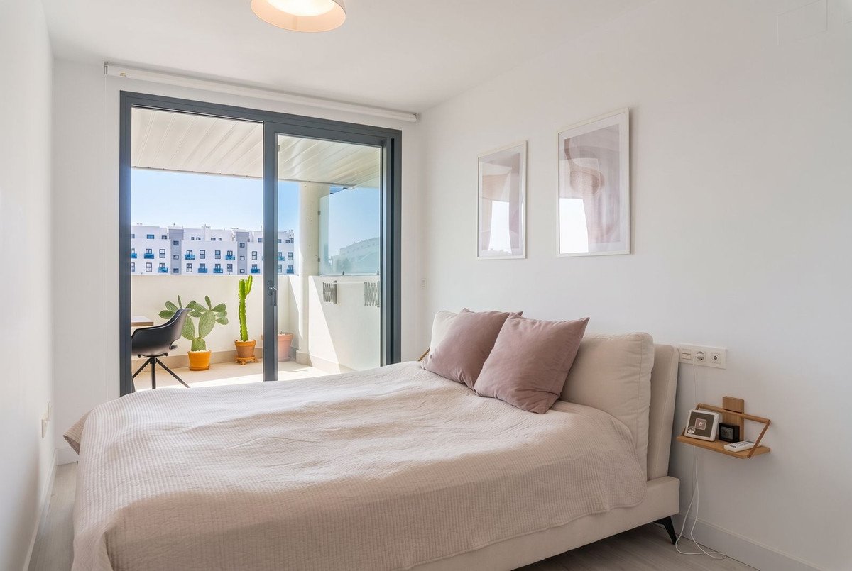 Modern bedroom with a bed, large sliding glass door leading to a balcony with plants and city view.