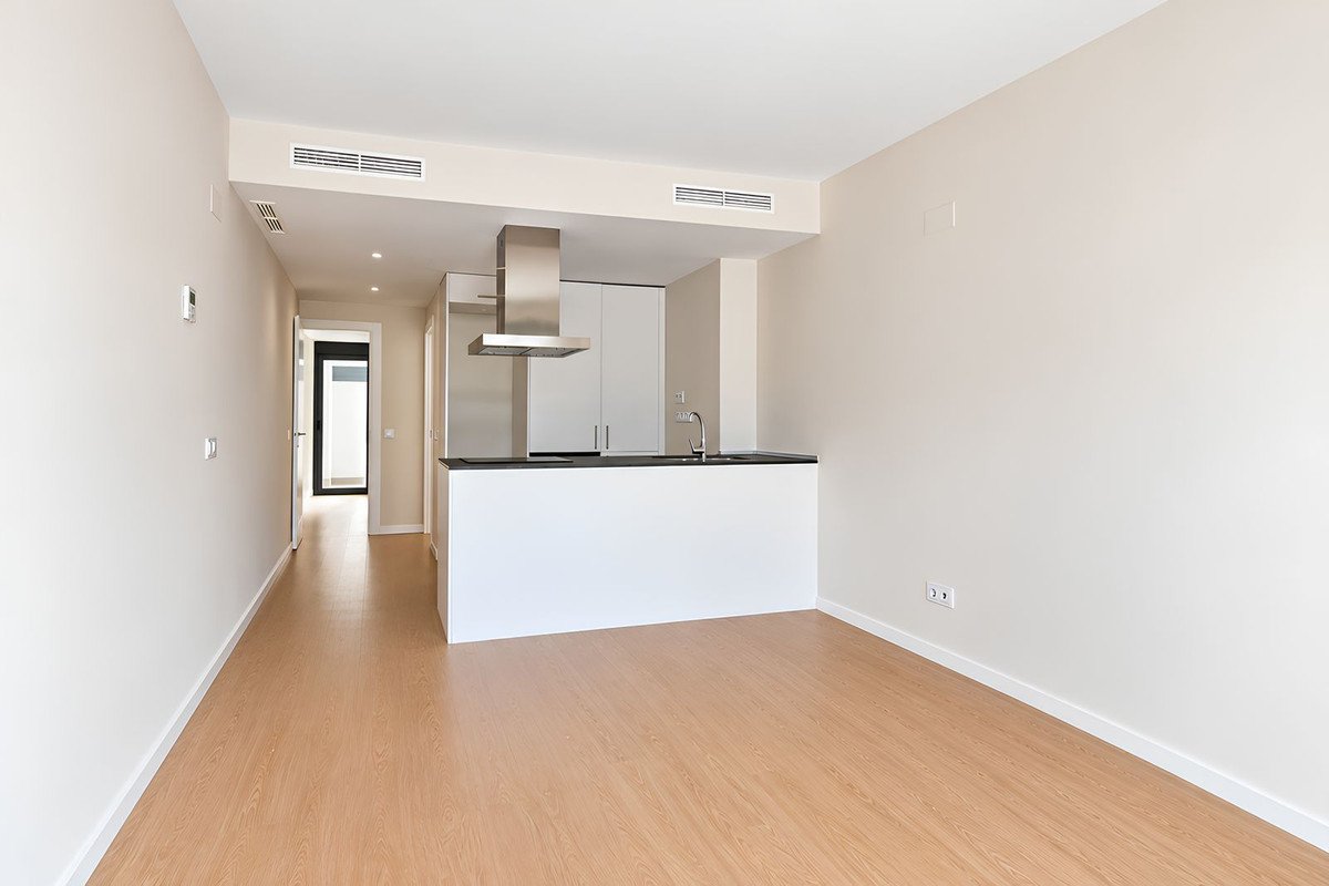 Modern kitchen with island and extractor hood, opening into a hallway and living space with light wood floors.