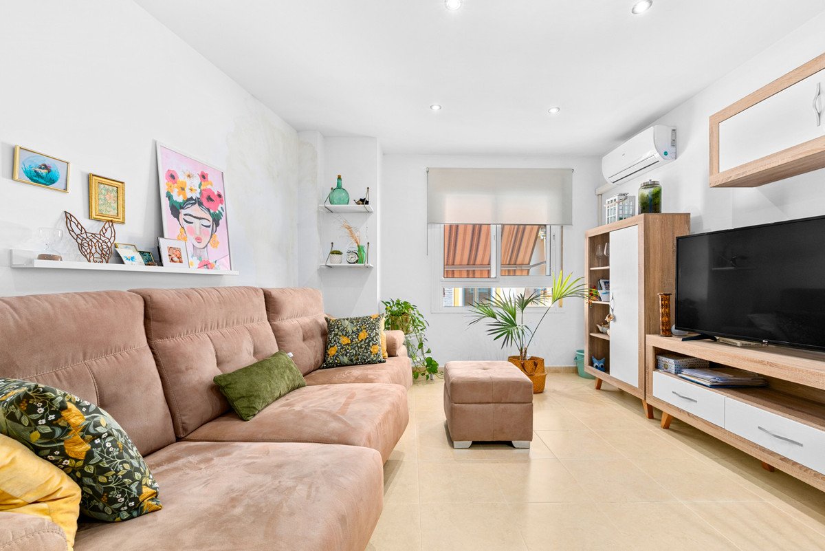A spacious living room with a large sectional sofa, a TV, and a window with blinds, decorated with artwork and plants.