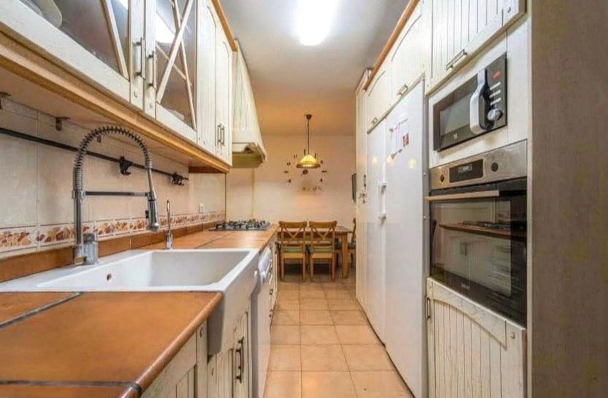 A compact kitchen with white cabinets, a farmhouse sink, and stainless steel appliances, leading to a small dining area.