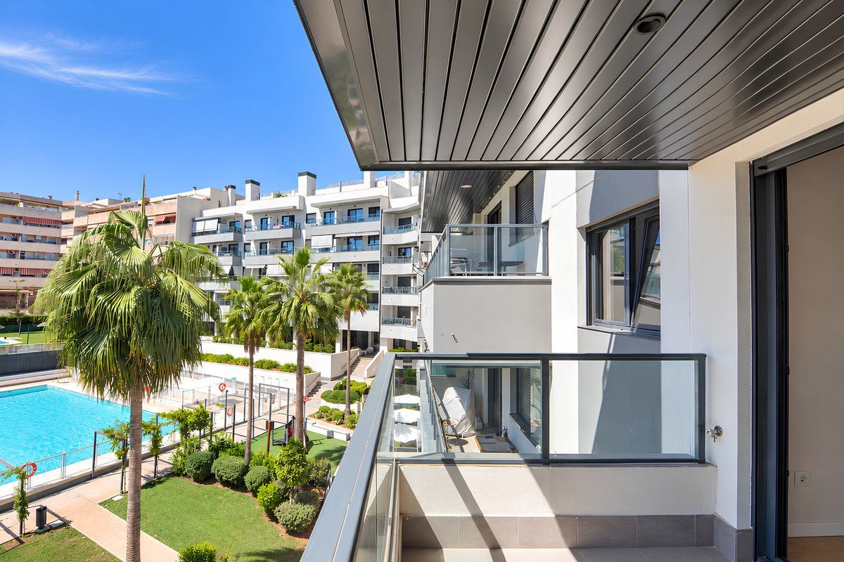 View from a modern balcony overlooking a swimming pool, lush gardens, and palm trees on a sunny day.