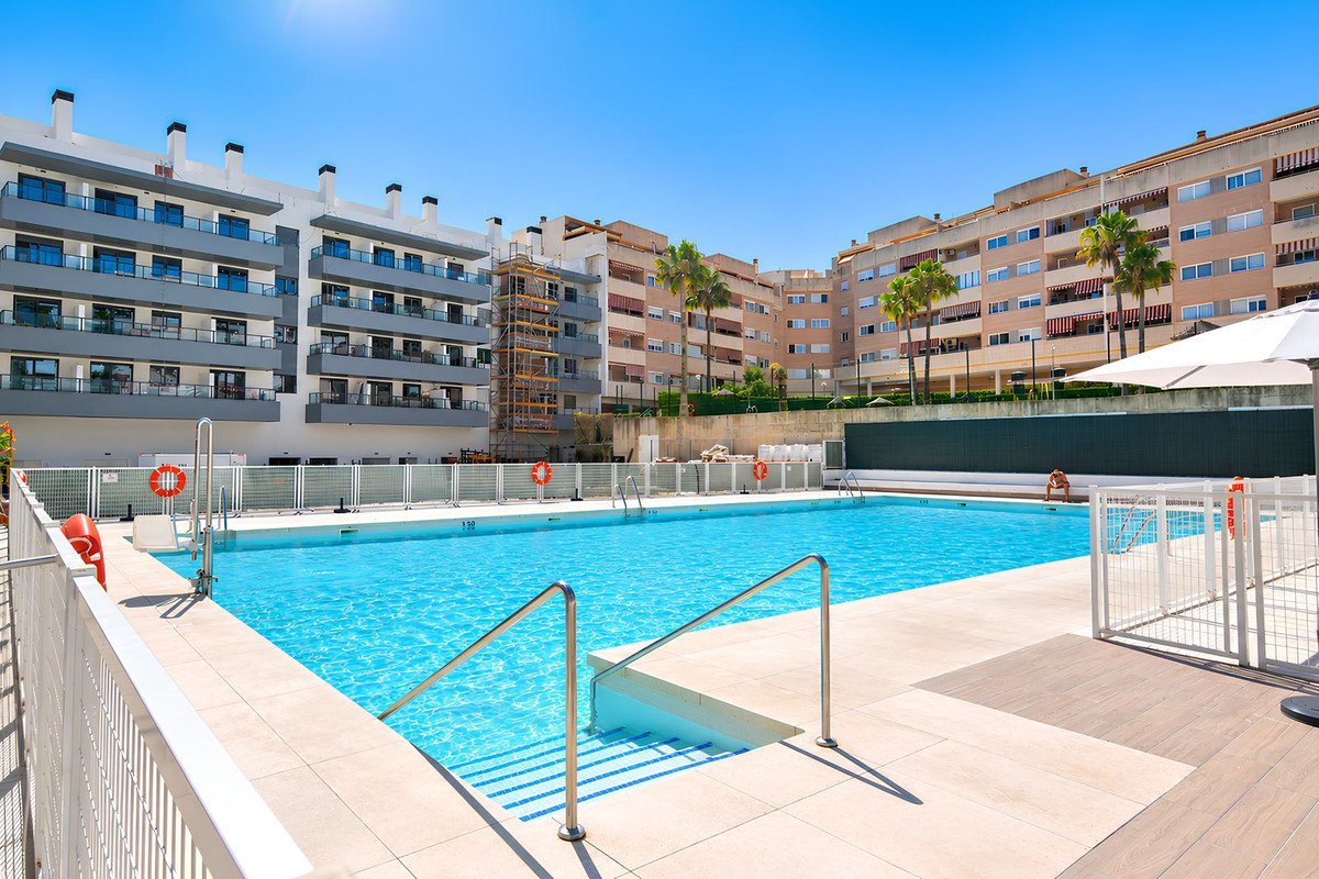 Bright outdoor swimming pool area with surrounding apartment buildings and palm trees under a clear blue sky.