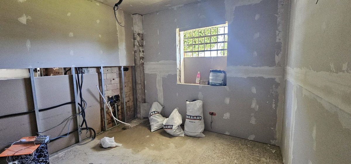 Interior room under construction with drywall, exposed studs, electrical wiring, and bags of building materials.