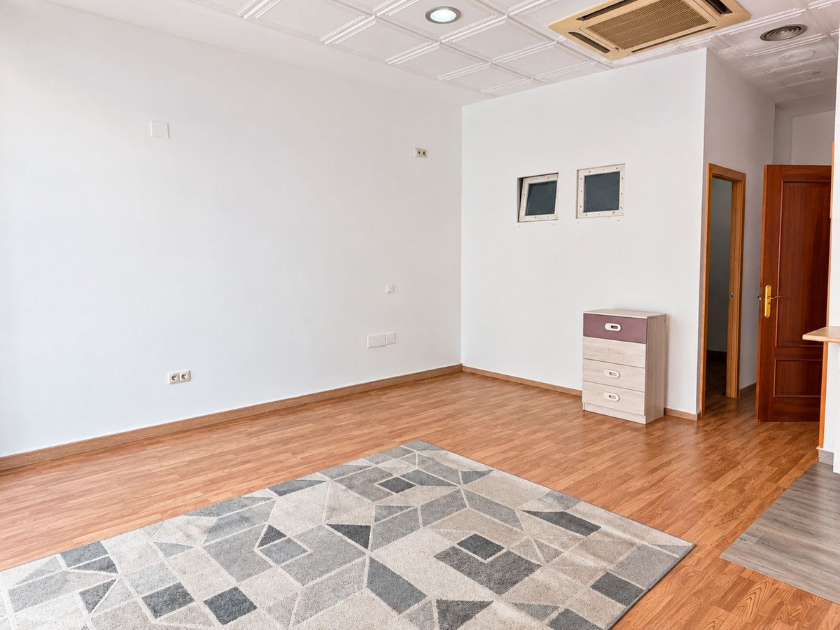 Empty living room with wooden floors, a patterned rug, air conditioning unit, and double doors leading to another room.
