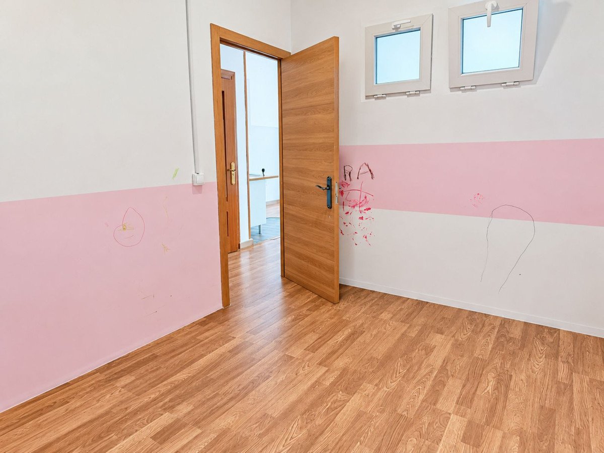 Empty room with hardwood floor, pink lower wall section, and two small windows. Open door reveals another room.