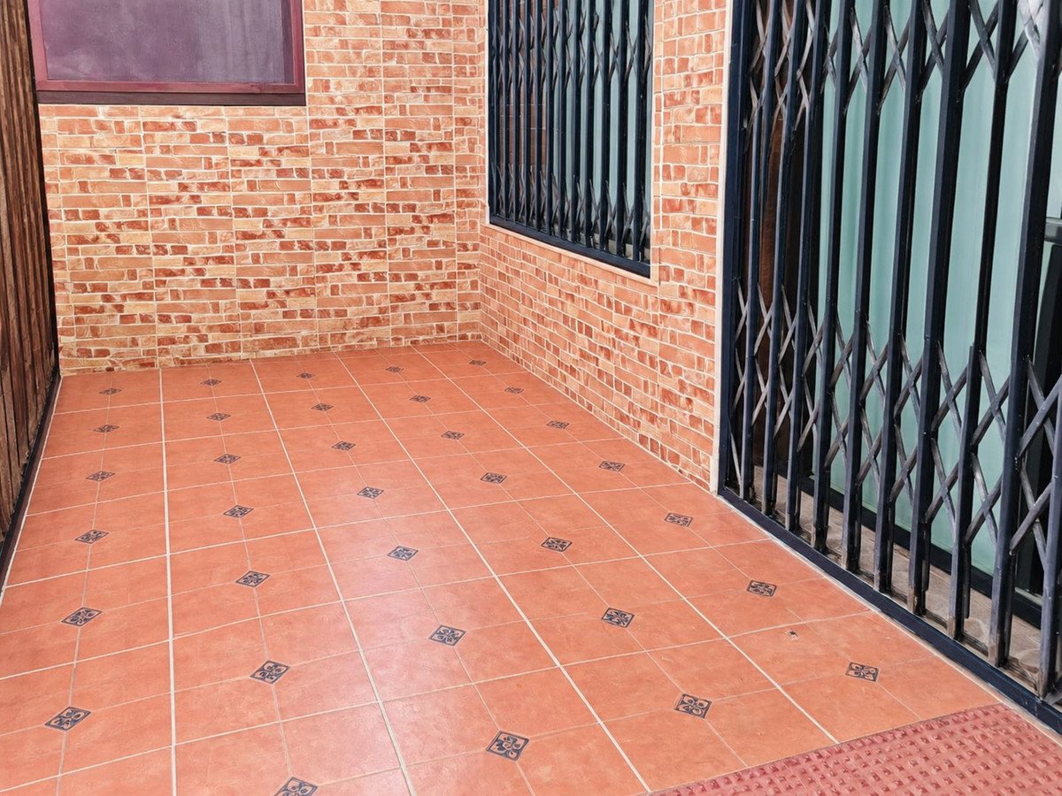 A tiled porch area with a decorative brick pattern wall and security gates, offering an outdoor space.