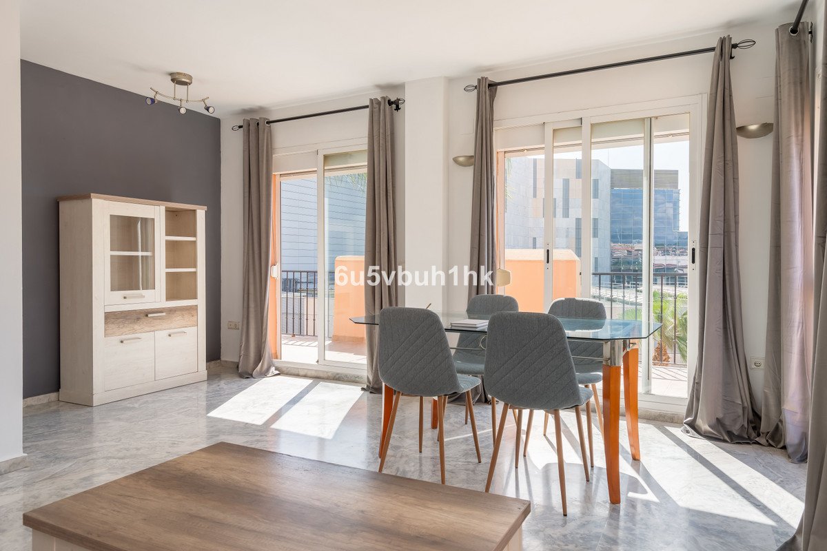 Dining area with a glass table and chairs, featuring a balcony with a view of buildings and sunlight streaming with natural light.