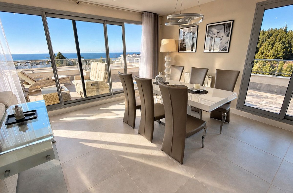 Modern dining room with white table and chairs, offering a stunning sea view and access to a spacious terrace.
