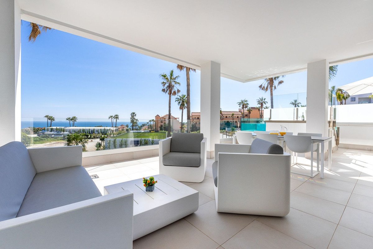 Modern terrace with lounge furniture and dining set overlooking the sea with palm trees.
