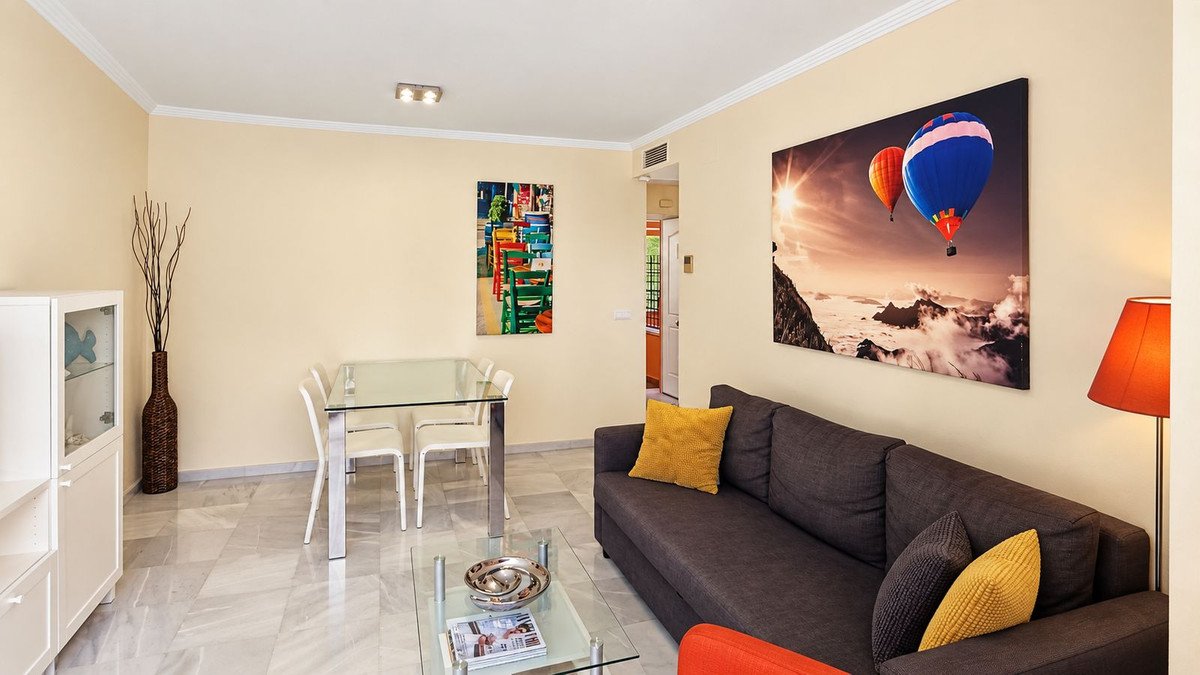 A modern living and dining room with a sofa, glass dining table, and contemporary artwork featuring hot air balloons.