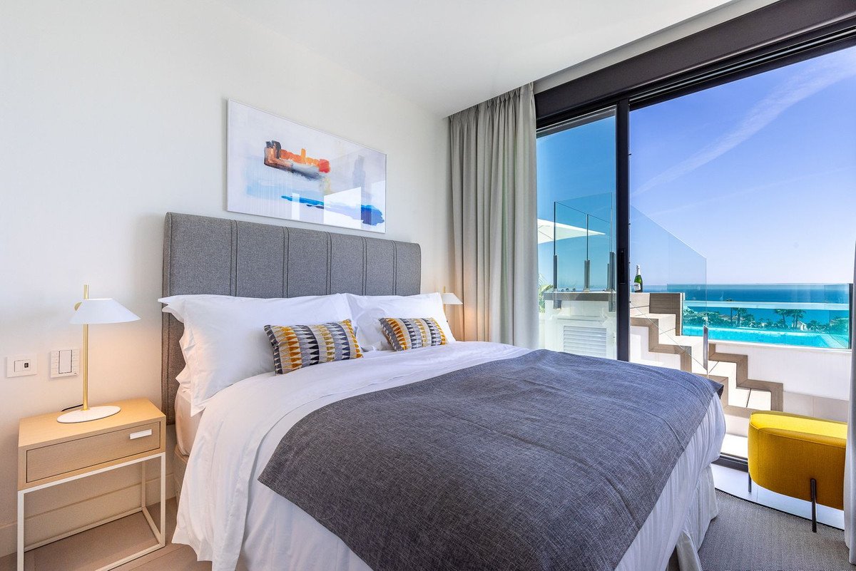 Bedroom with a large bed, modern art, and a stunning ocean view with an infinity pool.