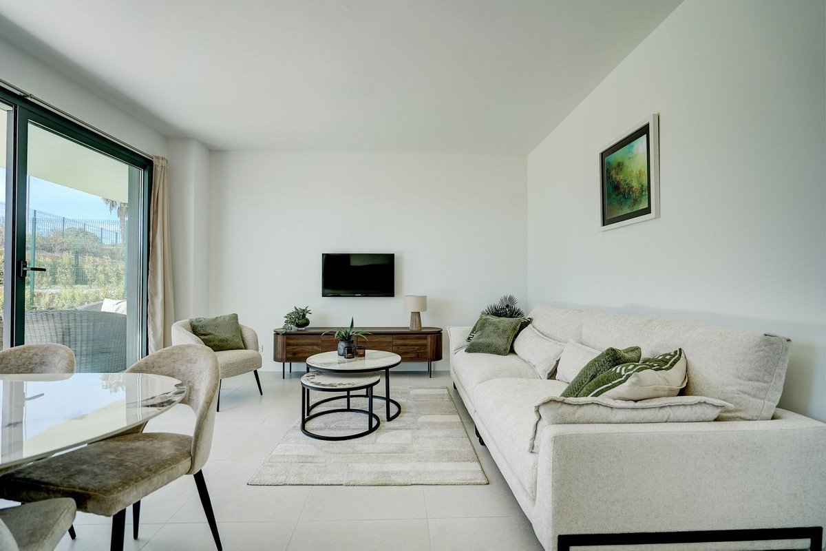 Modern living room with a comfortable sofa, coffee tables, TV, and large windows offering a garden view.